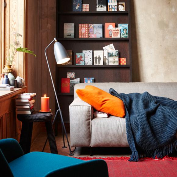 Wohnzimmer Deko Stehlampe modern offen Bücherregal Sofa Grau Kissen kuschelig Decke Arbeitstisch Bücher Orange Rot Blau-Wohnideen