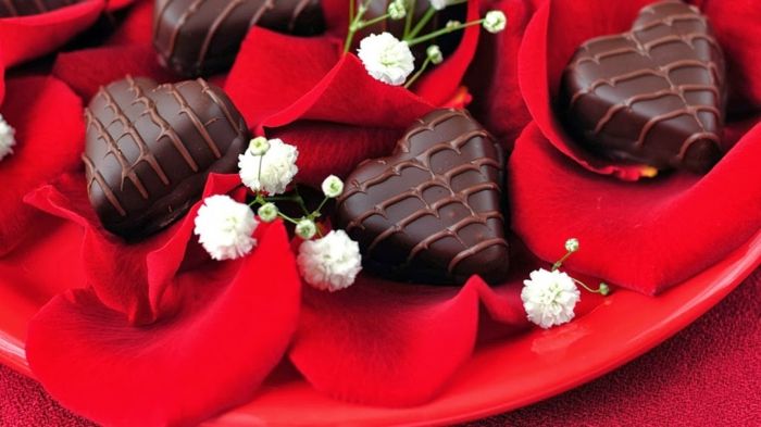 Pralinen in Herzform auf Rosenblättern-Romantische Stimmung mit passender Dekoration schaffen-Süßigkeiten Pralinen Schokolade Herzform Valentinstag Tisch Deko