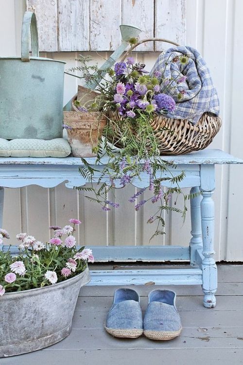 blauer Tisch Wiesenblumen Metallgefäß Geflechtkorb