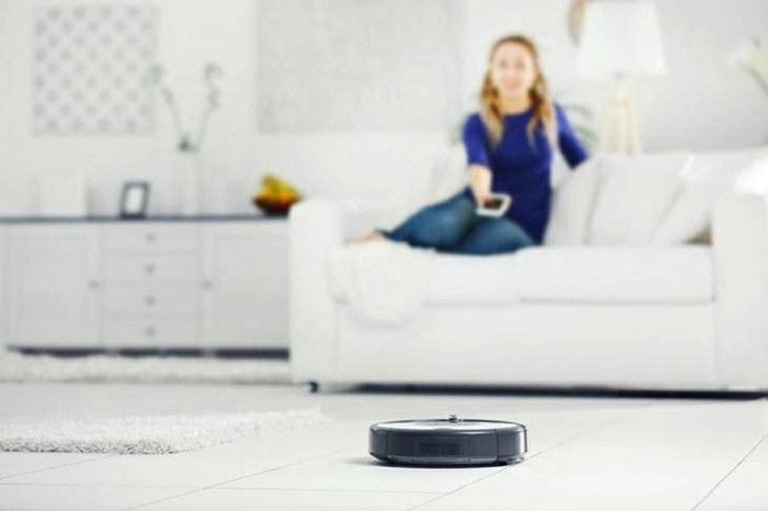 robot-vacuum-cleaner-cleans-the-room-while-woman-sits-on-the-couch