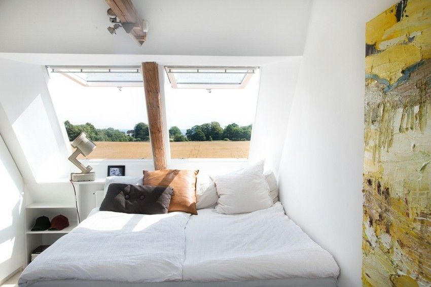 Schlafzimmer in weißen Farben mit Holzbalken und Fenster über dem Kopf großes Bild in warmen Farben
