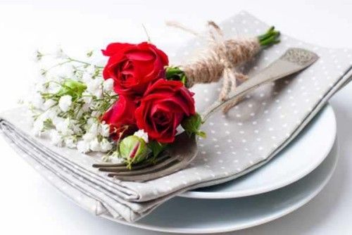 Festlich dekorierter Tisch rote Rosen auf Serviette weiße Porzellanteller Besteck
