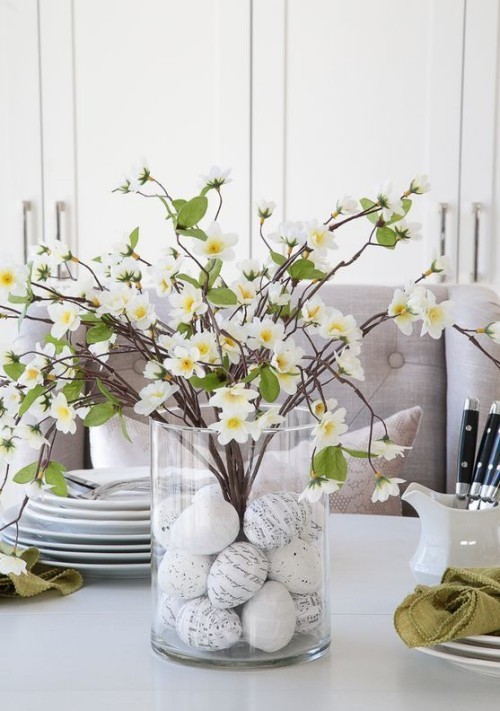 Blumendeko zu Ostern Vase aus durchsichtigem Glas mit verzierten Ostereiern und üppig blühenden Zweigen cooles und einfaches Ostern Mittelstück