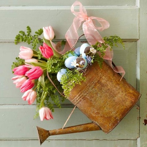 Blumendeko zu Ostern alte Vintage Gießkanne mit Grünpflanzen rosa Tulpen und blauen Eiern