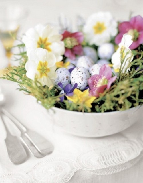 Blumendeko zu Ostern eine Schale mit Gras Frühlingsblüten und gefleckten Eiern in Pastellfarben