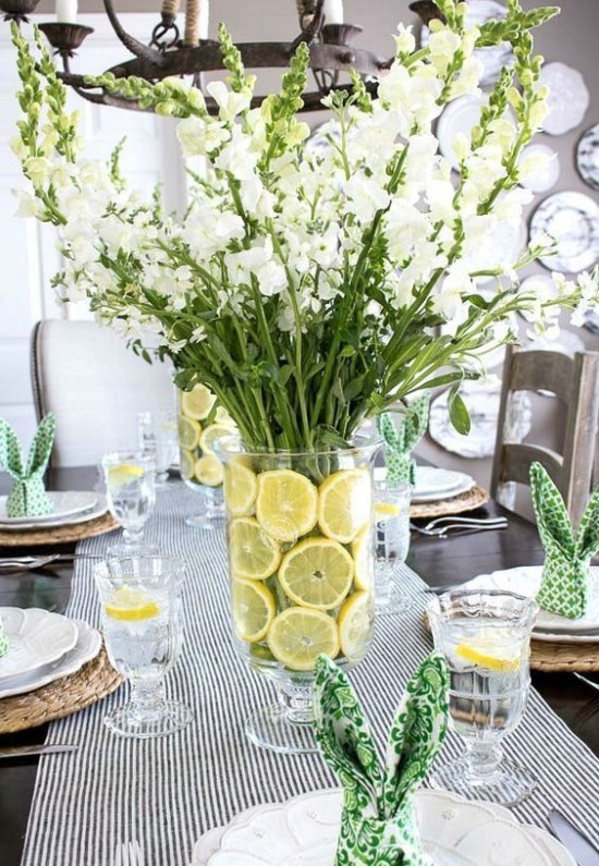 frühlingshafte Tischdekoration schöne weiße Blumen in Vase mit Wasser und Zitronenscheiben