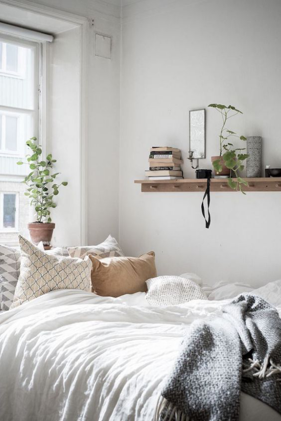 Schlafzimmer Ideen im Scandi Style Bett am Fenster viel Tageslicht beigefarbenes Kissen Regal aus hellem Holz