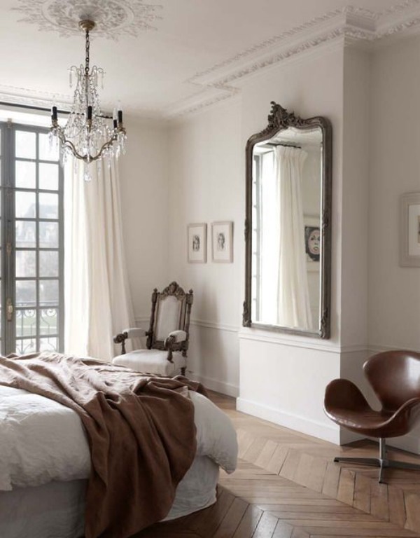 Pariser Chic im Schlafzimmer Parkettboden Spiegel gegenüber dem Schlafbett klassischer Sessel in der Ecke noch ein moderner links im Vordergrund Kristall-Kronleuchter Wurfdecke