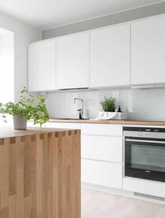 Skandinavische Küche rustikales Flair weiße Schränke Arbeitsplatte und Kücheninsel aus hellem Holz grüne Pflanzen als Blickfang