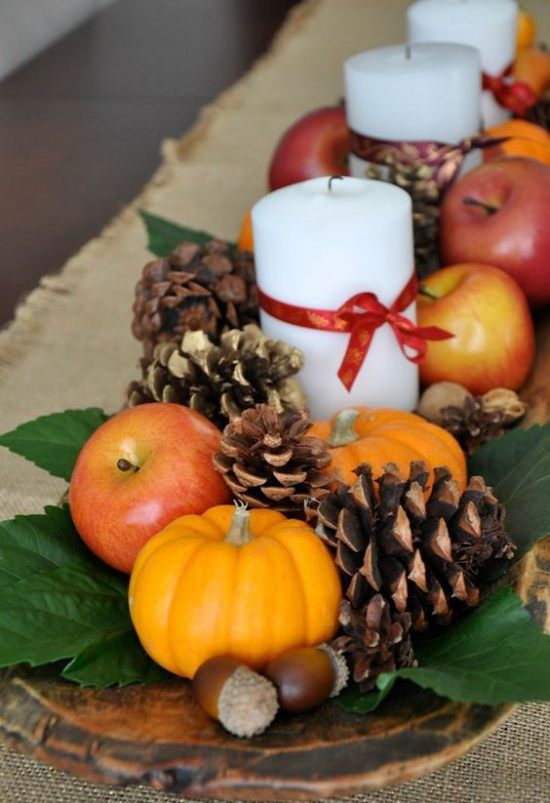 Herbstdeko mit Tannenzapfen auf ein Holztablett arrangiert Zapfen Eicheln kleine Kürbisse Äpfel weiße Kerzen mit roter Schleife