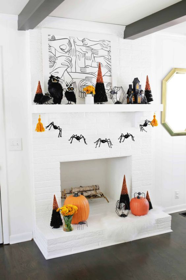 Halloween Deko im Wohnzimmer Kamin gruselig aber stilvoll dekorieren auf weißem Hintergrund wenig Deko schwarze Spinnen orange Kürbisse