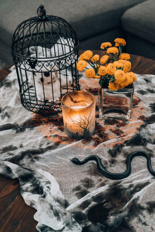 Halloween Deko im Wohnzimmer auf dem Kaffeetisch schwarze Schlange orange Akzente Teelicht Blumen Käfig