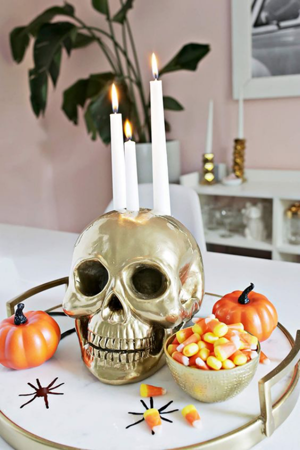 Halloween Deko im Wohnzimmer auf dem Kaffeetisch silberner Totenkopf weiße Kerzen orangefarbene Kürbisse milde Note