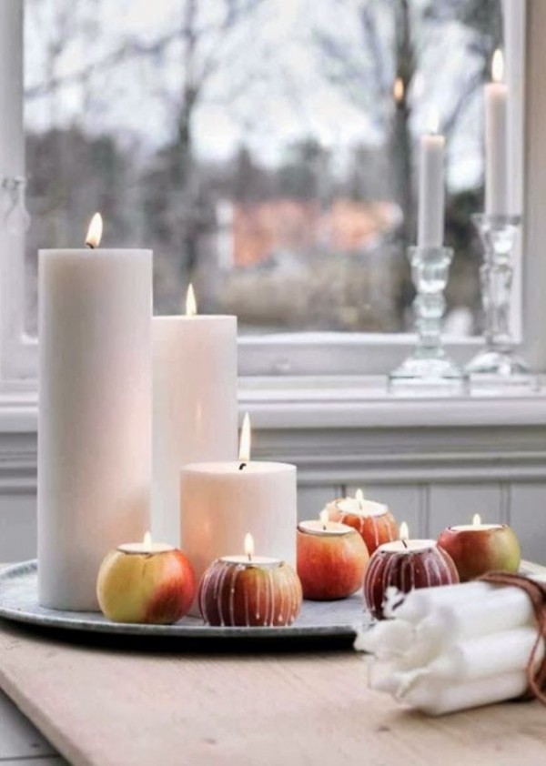 Skandinavische Herbstdeko zu Hause weiße Kerzen brennende Teelichter in Äpfeln auf dem Esstisch vor dem Fenster
