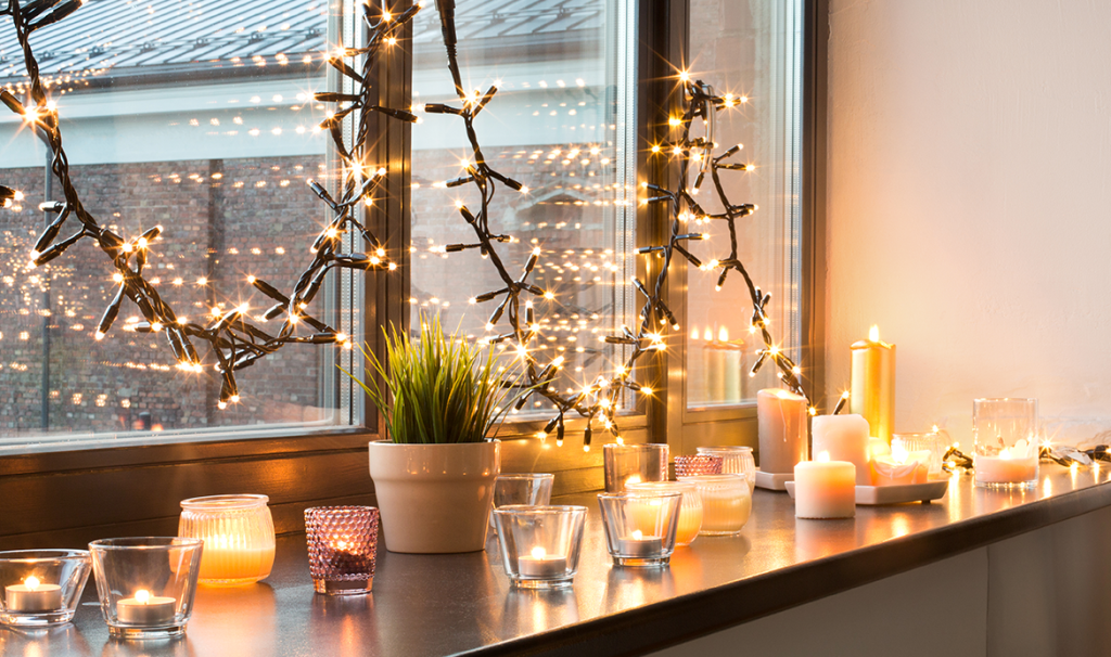 Hygge Dekoration und Weihnachtskonzept Kerzen die zu Hause in den Laternen und in der festlichen Girlande auf Fensterbrett brennen