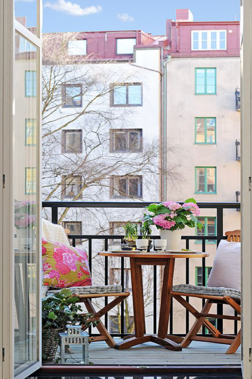 Balkon frühlingsfit machen mit Liebe zum Detail eingerichtet zwei Stühle runder Tisch Holz rosa blühende Blumen im Topf