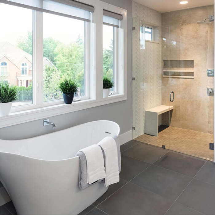 Badezimmer sanieren renovieren modernes stilvoll gestaltetes Bad weiße Badewanne weites Fenster viel Tageslicht Duschecke hinter Glaswand