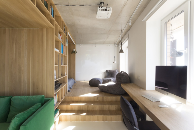 Modernes Homeoffice Arbeitsplatz vor dem Fenster eingebaute Bücherwand weiche Sitzmöbel im minimalistischen Industrial Style