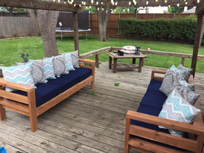 Gartenmöbel reinigen Veranda zwei Sofas aus Holz marineblaue Sitzkissen bunte Wurfkissen darauf Holztisch