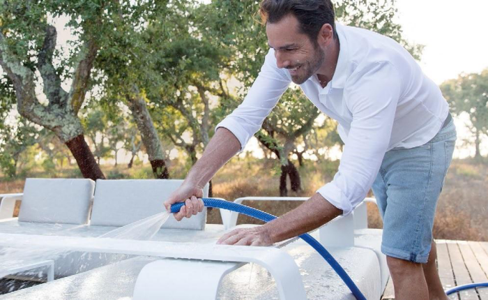 Gartenmöbel reinigen junger Mann mach Outdoor Möbel sauber mit dem Schlauch abspritzen