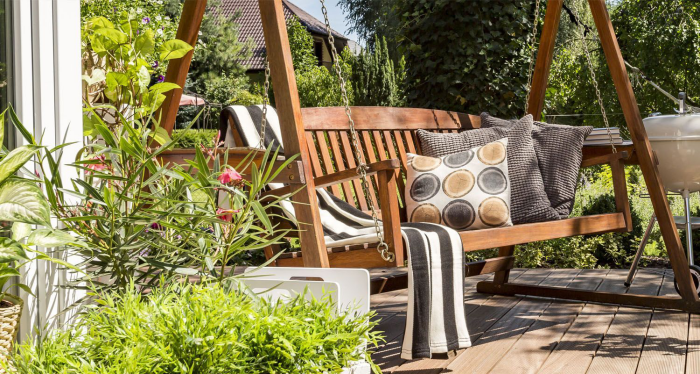 Moderne Terrassengestaltung trendige Einrichtungsideen Gartenschaukel aus Holz Decke Kissen viel Grün