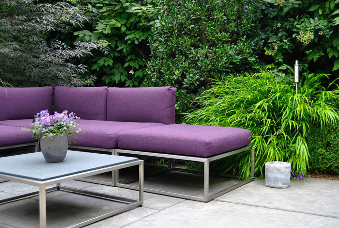 Moderne Terrassengestaltung trendige Einrichtungsideen schicke Sitzmöbel lila Polsterung viel Grün