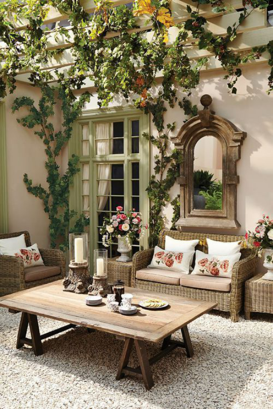 Outdoor Trends 2020 gemütliche Sitzecke im Freien erinnert an Wohnbereich Wandspiegel Holztisch Flechtmöbel weiche Kissen Grün Blumen