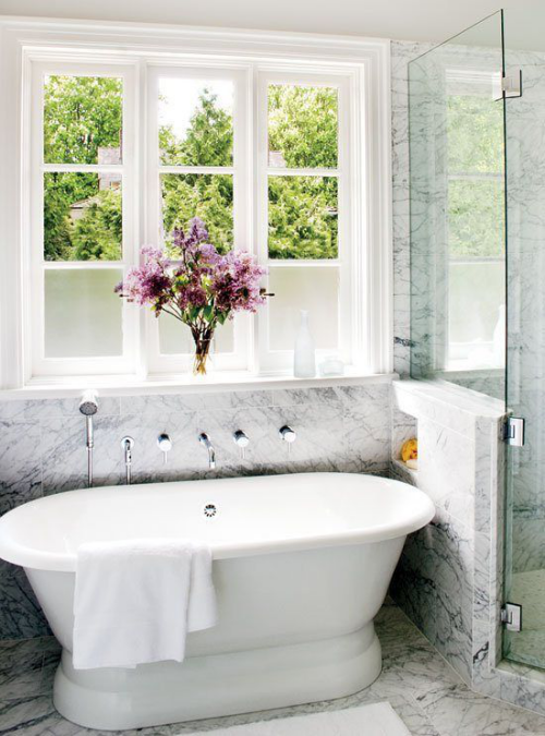 Marmor im Bad sehr einladend wirkend weiße Badewanne vor dem Fenstervase mit Blumen viel Tageslicht