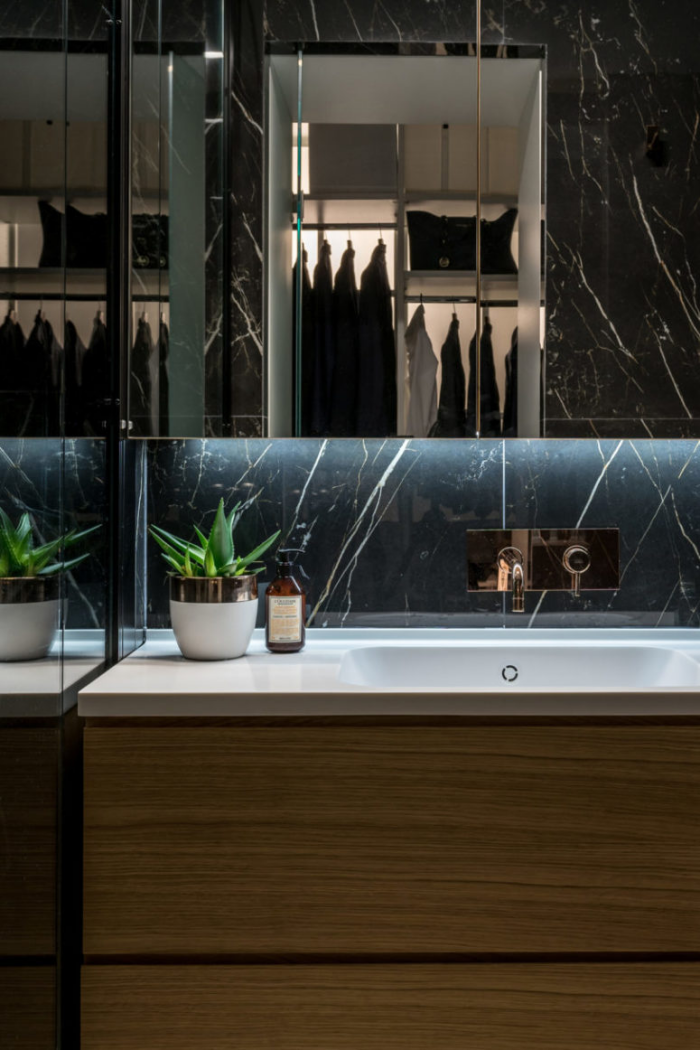 Minimalismus trifft Klassik luxuriöses Badezimmer schwarzer Marmor großer Spiegel grüne Topfpflanze Waschtisch Holzschrank Ankleideraum