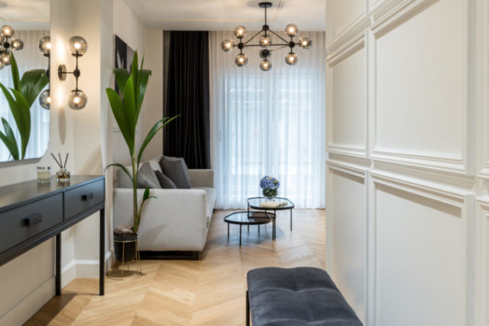 Minimalismus trifft Klassik offenes Raumdesign helle Farben vom Flur direkt ins Wohnzimmer graues Sofa links Konsolentisch Wandspiegel Grünpflanze