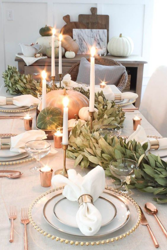 Herbstdeko mit Kürbissen festlich gedeckter Esstisch elegante Kerzen goldglänzendes Besteck grüne Blätter