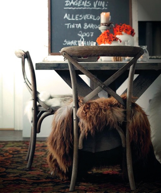 Kuschelige Sitzplätze Esszimmer schokoladenbraunes Kunstfell Stühle Esstisch schwarze Tafel im Hintergrund Vase mit Herbstblumen auf dem Tisch brennende Kerze