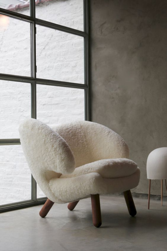 Kuschelige Sitzplätze bequemer Sessel mit weißem Kunstfell bezogen warm und kuschelig vor deckenhohem Fenster
