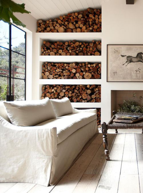 Brennholz richtig lagern geräumiges Wohnzimmer großes Fenster bequeme Couch eingebautes Regal neben dem Kamin