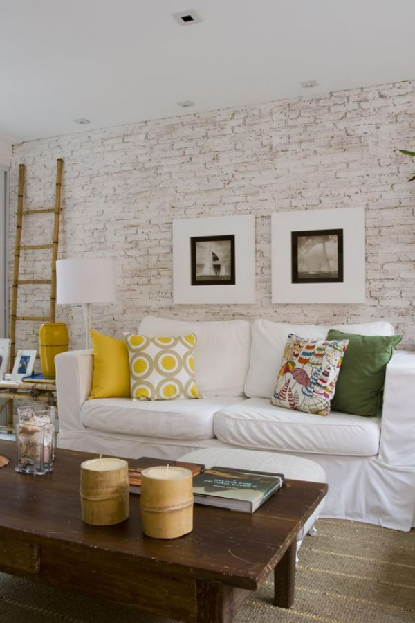 weiße Ziegelwand geräumiges Wohnzimmer weiße Couch Wurfkissen Kaffeetisch Kerzen Lampe Leiter an die Wand gelehnt