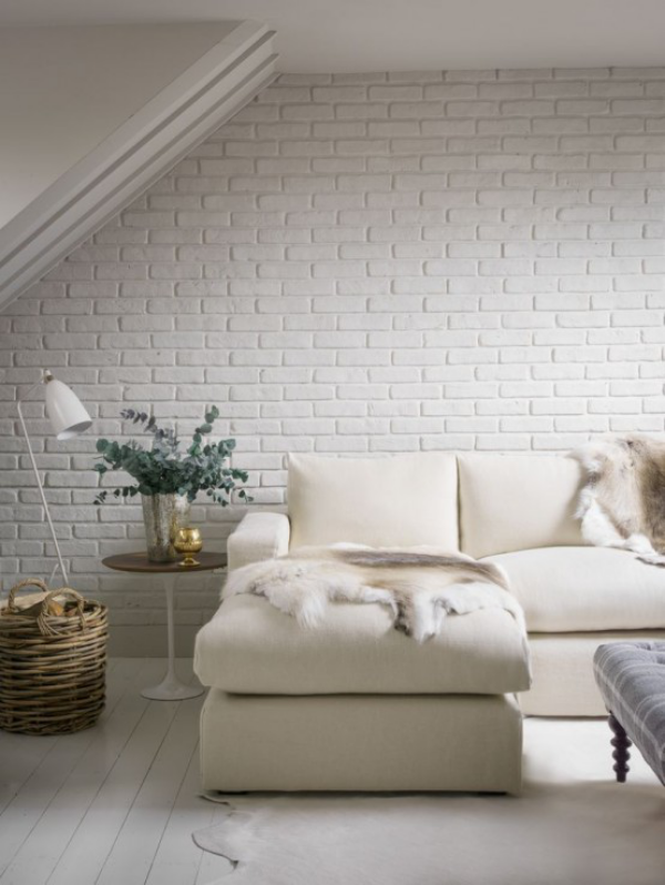 weiße Ziegelwand stilvoll gestaltetes Wohnzimmer unter der Dachschräge helle Ledercouch Pelze Teppich Lampe Tisch Vase mit grünen Zweigen