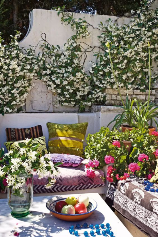 Veranda frühlingshaft gestalten kunterbunt zahlreiche blühende Pflanzen weiße Kletterpflanzen schöne Blumen in Töpfen bunte Kissen Decke
