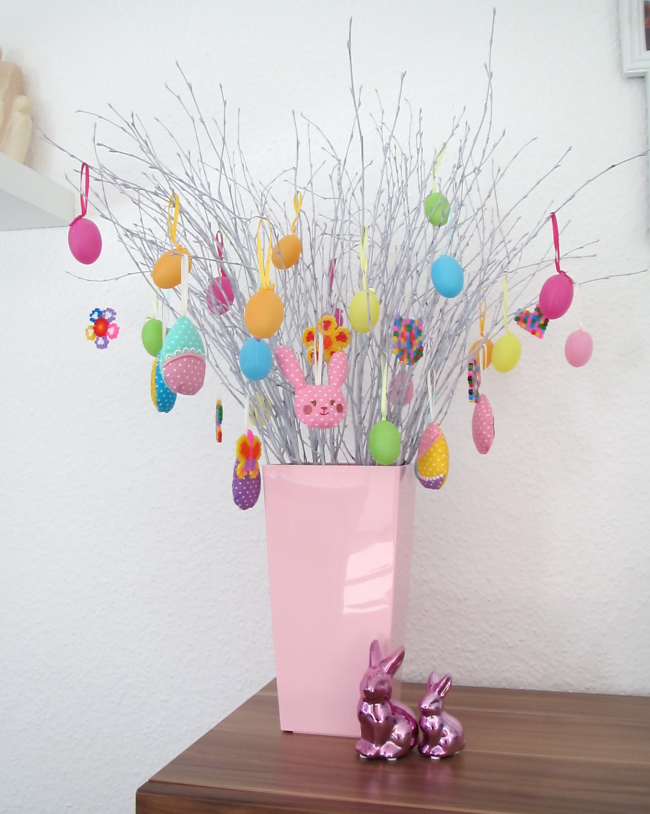 Osterstrauch schmücken rosafarbene Vase Zweige dekoriert mit farbenfrohen Eiern Anhänger aus Stoff Hasen