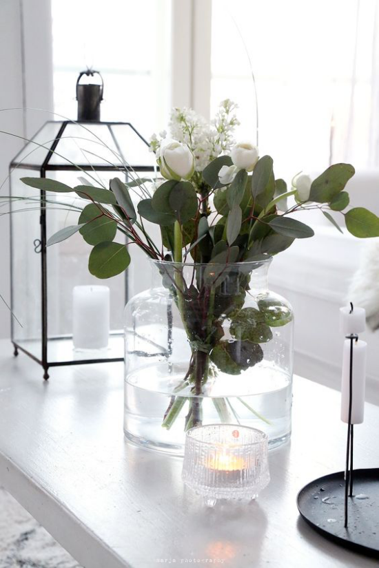 Schöne Blumenarrangements Glasgefäß weiße Tulpen Eukalyptusblätter Laterne weiße Kerzen daneben auf einem weißen Tisch