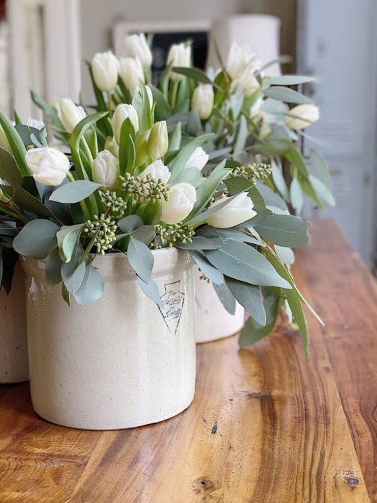 Schöne Blumenarrangements weiße Porzellangefäße weiße Tulpen etwas Grün auf Holzplatte