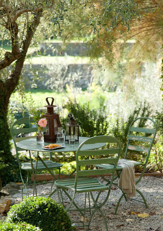 Essecke im Grünen alter Tisch zwei Laternen darauf Stühle aus Metall romantische Oase der Ruhe unter einem Baum