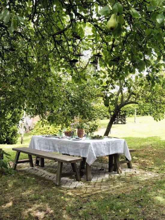 Essecke im Grünen großer Esstisch weiße Tischdecke zwei Sitzbänke beiderseits unter einem Baum viel Grün schöne Naturlandschaft