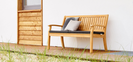 Gartenmöbel Trends 2021 bequeme Sitzbank im Freien aus Holz dunkle Sitzpolsterung zwei Kissen
