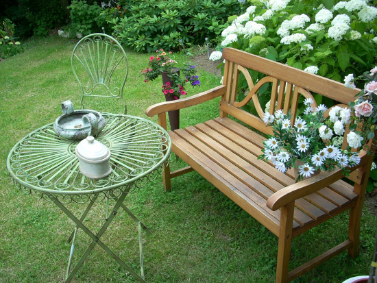 Gartenmöbel Trends 2021Sitzbank aus Holz runder Tisch aus Metall weiße Hortensien weiße Margeriten grüner Rasen schöne Umgebung