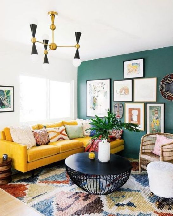 Gelbes Sofa eklektisches Raumdesign bunter Teppich grüne Akzentwand Bilder moderner runder Tisch aus schwarzem Metall