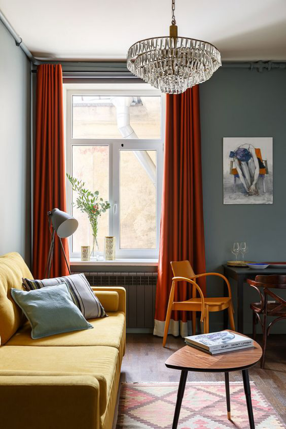 Gelbes Sofa fein gemusterter Teppich viele Farben schweißt alles zusammen rote Gardinen orangenfarbener Stuhl dunkelbrauner Tisch dunkle Wand