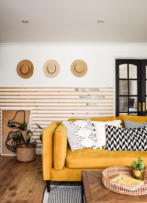 Gelbes Sofa halbgestreifte Wand Hüte als Wanddekoration Kissen in unterschiedlichen Mustern weiß grau schwarz