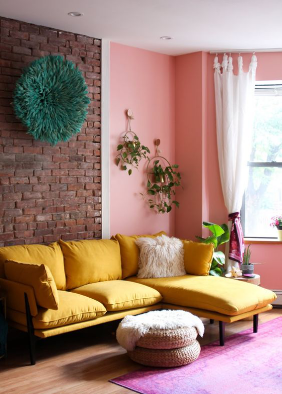 Gelbes Sofa schickes Design Kissen Ziegelwand als Akzent daneben rosa Wandfarbe Fenster leichte Gardinen