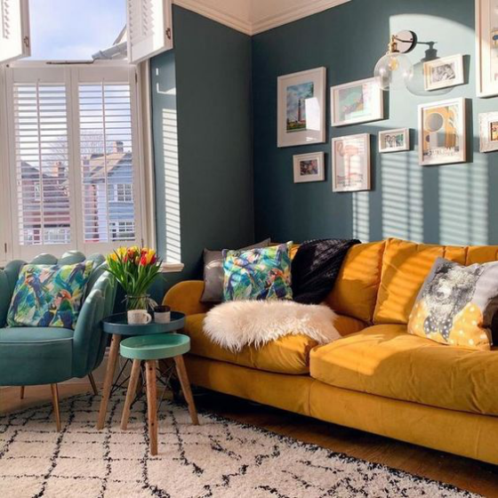 Gelbes Sofa schickes Wohnzimmer dunkelgrüne Akzentwand Sessel Wandbilder Beistelltische Vase mit Tulpen