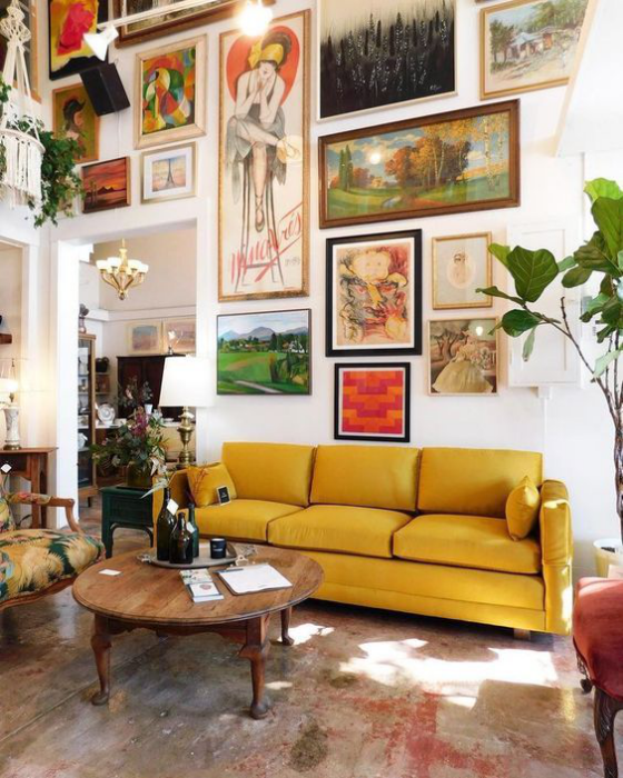 Gelbes Sofa zahlreiche Bilder an der Wand darüber niedriger runder Tisch grüne Topfpflanze rechts